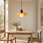 Yellow disc-shade pendant light with black body above a timber dining table